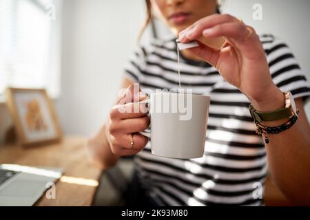 Glück findet man in einer Tasse Tee. Eine unkenntliche Frau genießt eine Tasse Tee, während sie in ihrem Studio woking. Stockfoto