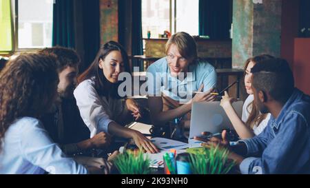 Junge Männer und Frauen Kollegen schauen sich Papiere an, die auf dem Tisch liegen, und reden über Ideen. Teamwork, modernes Büro-, Informations- und Mitarbeiterkonzept des Unternehmens. Stockfoto