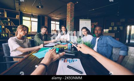 Der Firmeninhaber spricht mit seinen Mitarbeitern bei einem Treffen am Tischkopf, während eine Gruppe junger Menschen ihn anschaut und ihm zuhört. Management- und Geschäftskonzept. Stockfoto