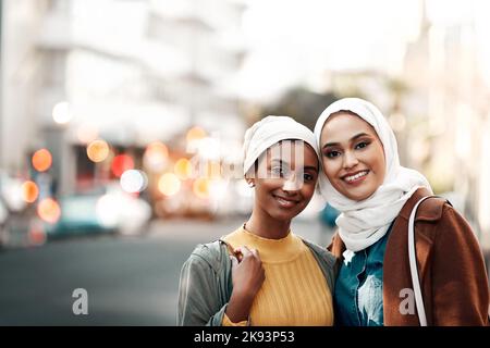 Beste Freunde bis zum Ende. Zwei attraktive junge Frauen tragen Kopftücher und stehen zusammen, während sie gemeinsam durch die Stadt Touren. Stockfoto