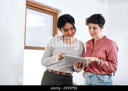 Was halten Sie davon? Zwei attraktive junge Geschäftsfrauen stehen im Büro zusammen und nutzen ein Tablet. Stockfoto
