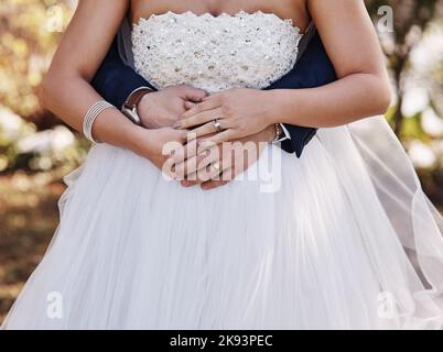 Weve beschloss, unser Leben miteinander zu teilen. Ein unkenntlich gebratenen Bräutigam umarmte seine Braut von hinten, während er an ihrem Hochzeitstag draußen stand. Stockfoto