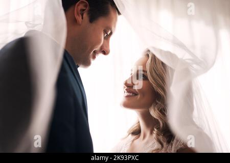 Immer dein, immer mein, immer unser. Ein glückliches junges Paar, das drinnen steht und sich nach ihrer Hochzeit liebevoll anschaut. Stockfoto
