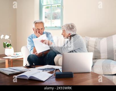 Finanzieller Stress fordert ihren Tribut für ihre Ehe. Ein älteres Paar, das eine Meinungsverschiedenheit hat, während es zu Hause Papierkram durchläuft. Stockfoto