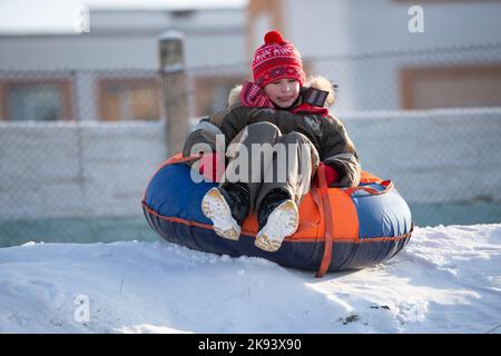 Ein glücklicher Junge in der Luft auf einem Schlauchschlitten im Schnee. Ein Junge rutscht im Winter einen Hügel hinunter. Stockfoto