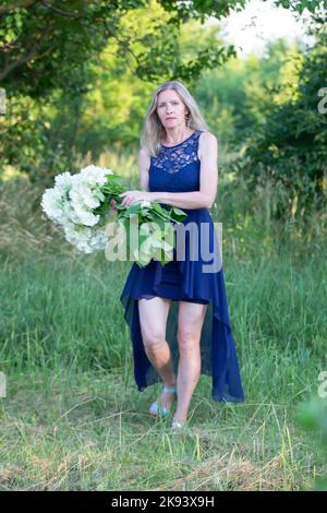 Eine ältere Frau, schön und gepflegt, spaziert mit einem Blumenstrauß im Garten. Stockfoto