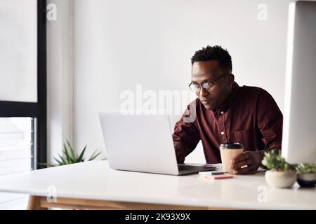 Ein hübscher junger Geschäftsmann, der alleine sitzt und im Büro an seinem Laptop arbeitet. Stockfoto