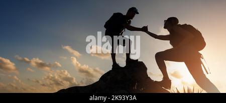 Wanderer-Team Klettern auf Bergklippe bei Sonnenuntergang. Geben helfende Hand. Teamarbeit und Assistenz-Konzept. Banner mit Kopierraum Stockfoto