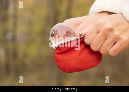 Rote leere Brieftasche mit einer transparenten Glaskugel im Blick auf den Planeten in den Händen eines Mädchens auf der Straße, weltweiter Geldmangel Stockfoto