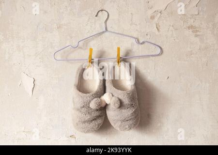 Graue, weiche Hausschuhe für Frauen, die an einem Kleiderbügel an einer alten weißen Wand hängen Stockfoto