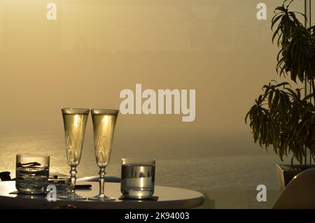Zwei Gläser Champagner und Wasser auf einem Hintergrund bei Sonnenuntergang mit goldenem Farbton, der Romantik, Paare, Feiern, Feiern evoziert Stockfoto