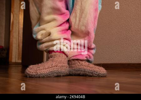 Kinderfüße in warmen Stricksocken auf dem Boden des Hauses im Winter, kalter Boden Stockfoto