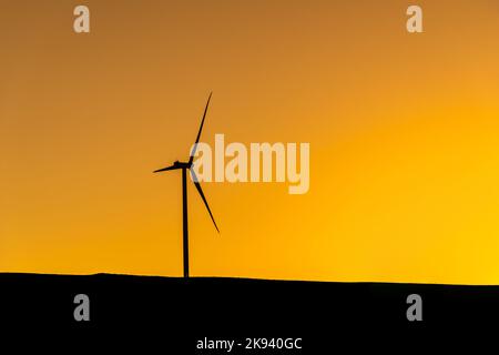 Windturbine, die bei Sonnenuntergang auf einem Hügel steht und Strom erzeugt Stockfoto