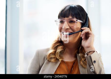 Hallo, wie kann ich Ihnen helfen? Eine attraktive junge Geschäftsfrau, die tagsüber mit ihrem Headset posiert, während sie in ihrem Büro ist. Stockfoto