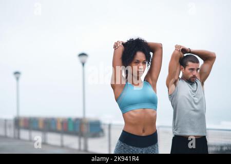 Konzentriert sich darauf, ihren Körper locker und limber zu machen. Zwei sportliche junge Menschen dehnen sich beim Training im Freien. Stockfoto