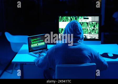 Sichern Sie alles, was Sie können, bevor es zu spät ist. Rückansicht eines männlichen Hackers, der im Dunkeln einen Computercode knackt. Stockfoto
