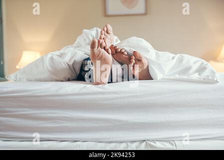 Wir bleiben den Rest des Tages im Bett. Ein unbekanntes Paar stockt unter die Laken, während es zu Hause zusammen im Bett liegt. Stockfoto