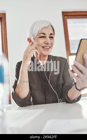 Eine attraktive, reife Geschäftsfrau, die Nachrichten auf ihrem Handy hört, während sie im Büro sitzt. Stockfoto