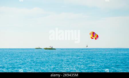 Herrliche Aussicht auf den bunten Parasailflügel, der von einem Boot gezogen wird, im strahlend blauen Meer, Alanya, Türkei. Hochwertige Fotos Stockfoto