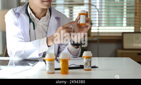 Abgeschnittene Aufnahme eines Arztes, der auf Medikamentenflaschen mit leerem Etikett zeigt. Medizin, Gesundheit und Menschen Konzept Stockfoto