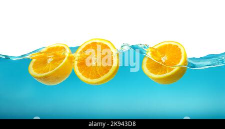 Frische orange Früchte fließen in blaue Wasserwelle mit Spritzer isoliert auf weißem Hintergrund. Stockfoto