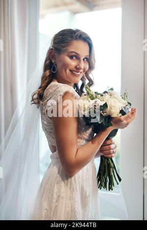 Und so beginnt das Abenteuer. Ein Porträt einer attraktiven jungen Braut, die allein in der Garderobe steht und ihren Blumenstrauß hält. Stockfoto