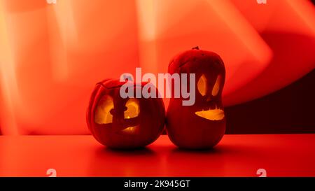 Zwei Jack-o-Laternen leuchten im Dunkeln auf rotem Hintergrund. Halloween Dekoration. Stockfoto