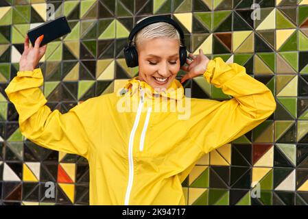 Das sind solche Tanzlieder. Eine attraktive junge Frau, die an einer Wand steht und Musik von ihrem Handy über Kopfhörer hört. Stockfoto