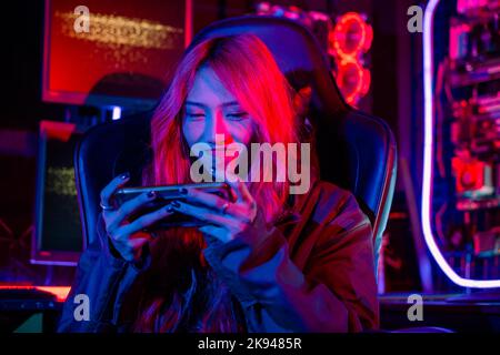 Asiatische Frau Live-Stream Sie spielen Videospiel über Smartphone zu Hause Neon Lichter Wohnzimmer, Gamer spielen Online-Spiel-Anwendung auf Handy tragen Stockfoto