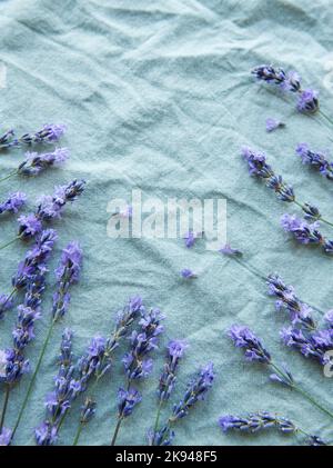 Lavendel blüht und hinterlässt einen kreativen Rahmen auf einem textilen Hintergrund. Draufsicht, flach liegend. Florale Komposition Stockfoto
