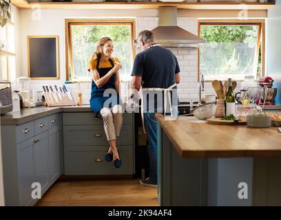 Paar, Wein und Kochen in der Küche, glücklich und reden während der Bindung, Gespräch und zu Hause. Senior, Mann und Frau im Ruhestand mit Glas, Essen und Stockfoto