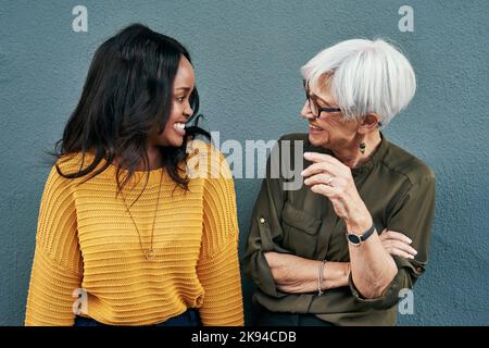 Verschütten Sie bereits die Bohnen. Zwei fröhliche Geschäftsfrauen, die im Freien gegen eine Wand stehen, diskutieren. Stockfoto