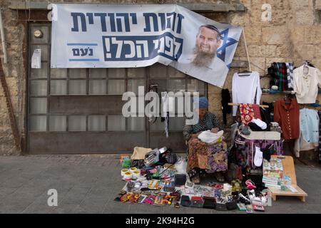 Ein israelischer Straßenhändler sitzt unter einem Wahlkampfplakat für die rechtsextreme orthodoxe jüdische politische Partei Noam, auf dem ihr Führer AVI Maoz mit einer Beschriftung mit der Aufschrift „Jüdische Identität vor allem“ dargestellt ist, und wird am 25. Oktober 2022 in Jerusalem, Israel, in der Straße Jaffa gezeigt. Öffentliche Meinungsumfragen zeigen deutliche Unterstützung für die religiöse Zionismus-Partei, die vor den Parlamentswahlen im November 1 mit der rechtsextremen Jewish Power zusammenläuft Stockfoto