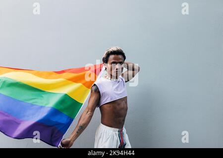 Junger Mann mit Regenbogenfahne, der im Freien auf die Kamera schaut Stockfoto