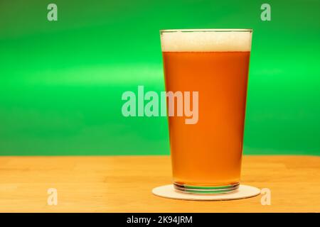 Volles Shaker Pint Glas Amber Ale oder Bier auf Holztisch mit grünem Hintergrund Stockfoto