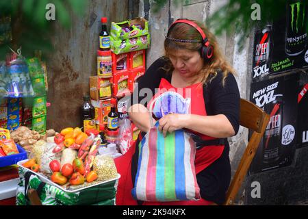 Der Blick auf eine Frau, die auf dem Bürgersteig sitzt und Waren verkauft, während sie Musik in La Boca hört Stockfoto