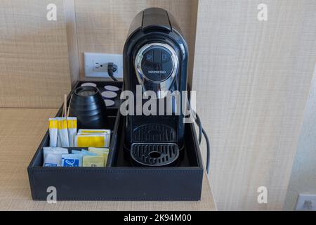 Nahaufnahme der Kapselkaffeemaschine mit Zubehör auf dem Tisch im Hotelzimmer. Stockfoto