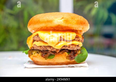 Queso Double Decker Brioche Burger in einem Café mit üppigem grünem Hintergrund. Stockfoto