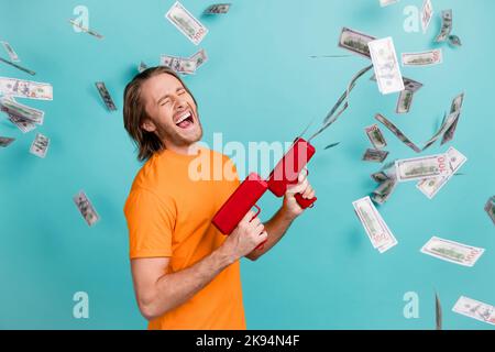 Foto von cool schöner Mann tragen orange T-Shirt Schießen Geld Pistole Geld fliegen isoliert türkisfarbenen Hintergrund Stockfoto