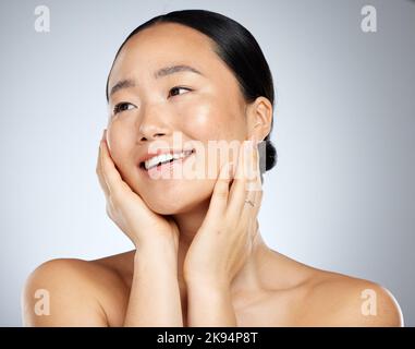 Asiatische Frau, Gesichtsglühen und Hautpflege Routine mit Händen berühren Wangen auf grauen Studio-Hintergrund. Lächeln, glücklich oder Beauty-Modell in gesunder Wellness Stockfoto