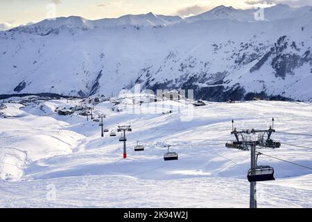 Gondelbahn im Skigebiet mit verschneiten Bergen im Hintergrund. Moderner Skilift mit Funitels und Stütztürmen hoch in den Bergen Stockfoto