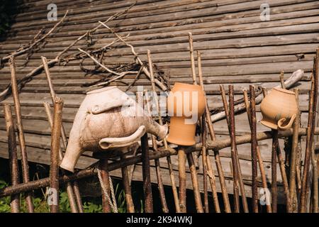 Alte Tontöpfe hängen einfach an einem Weidenzaun. Ukrainische ethnische Gerichte, traditionelle Kultur der Ukraine Stockfoto