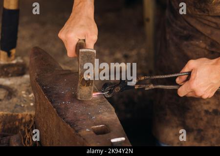 Ein Schmied schmiedet mit einem Hammer von Hand glühend heißes Metall auf einem Amboss Stockfoto