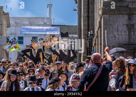 Schulkinder, die große Figuren von Rude Boys in Papierform bei der Parade zum Mazey Day im Rahmen des Golowan Festivals tragen Stockfoto