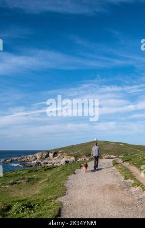 Ein Mann, der mit seinem Hund auf einem Küstenwanderweg in Richtung Towan Head in Newquay in Cornwall in England im Vereinigten Königreich läuft. Stockfoto