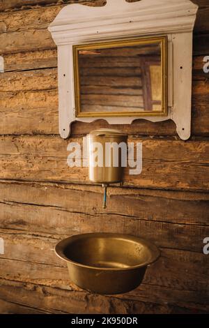 Vintage-Aufnahme eines alten Metallwaschbeckens und Spiegels in einem Holzhaus im Dorf Stockfoto