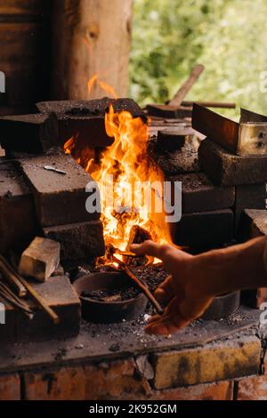 Ein Schmied härtet Stahl bei hohen Temperaturen in einem hausgemachten Ofen im Dorf aus Stockfoto