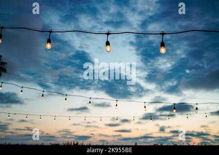 Outdoor String Lichter in schönen blauen und orangen Sonnenuntergang Himmel. Chill Vibe Copy Space Hintergrund Stockfoto