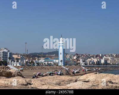 Eine Gruppe von Menschen genießen ihren Sommerurlaub am Strand in der Nähe der Mohammed VI Moschee in Fnideq Stockfoto