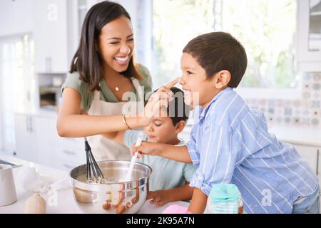 Familie Backen und Mutter lehrt Kinder, Kuchen in der Küche ihres Hauses zu backen. Fröhliche Latino-Kinder und Frauen spielen, kochen und lachen zusammen Stockfoto